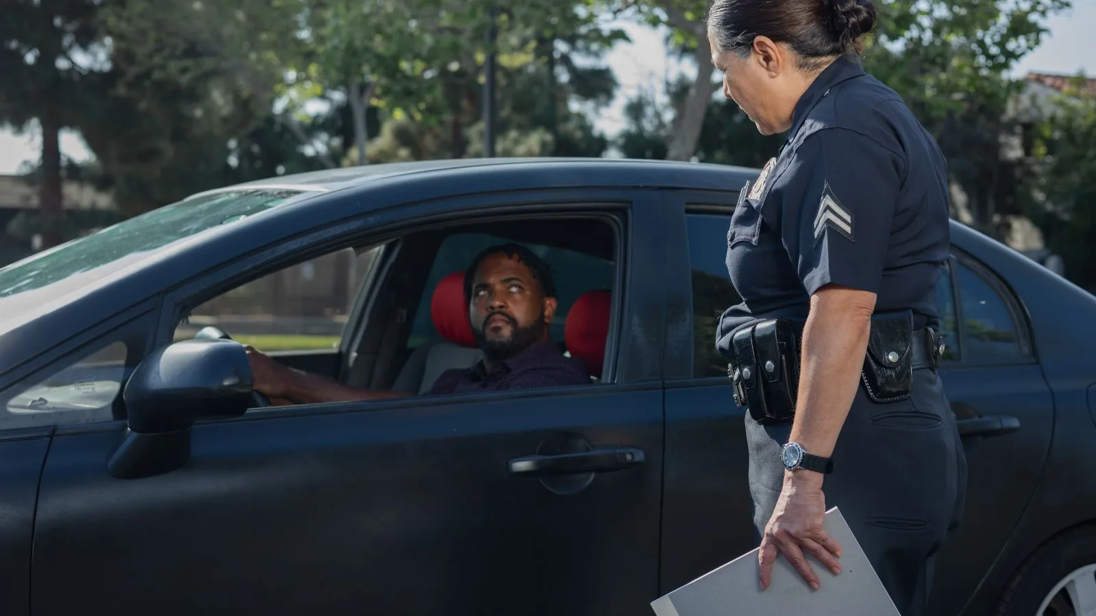 A policewoman discusses a traffic violation with a driver on a sunny day.