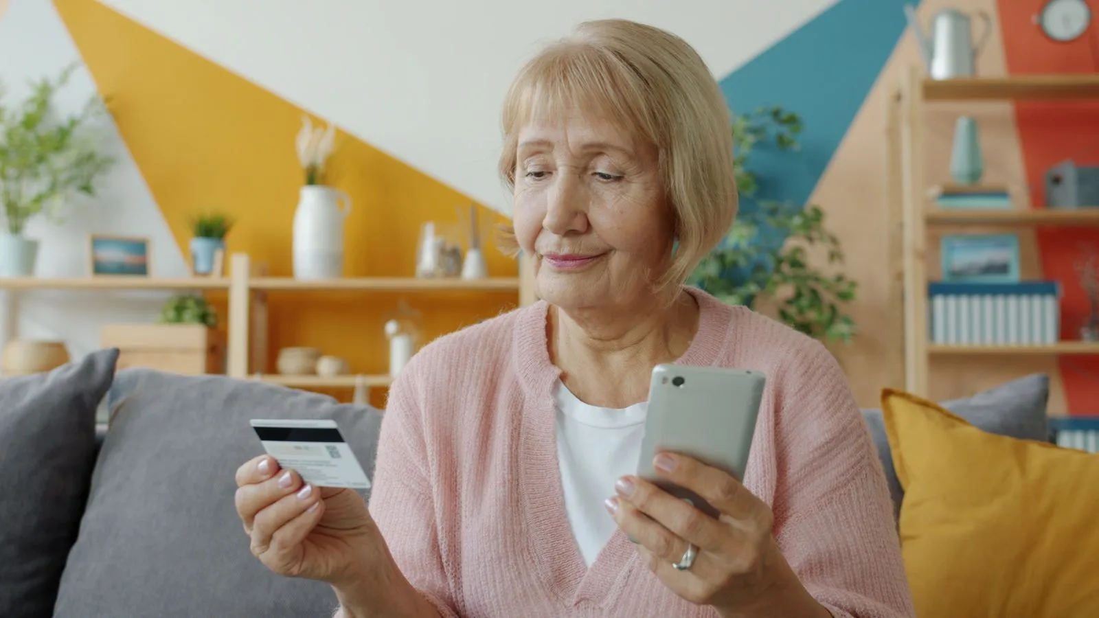 Elderly woman using smartphone and credit card for online shopping at home.