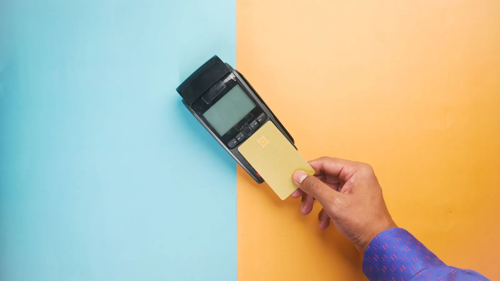 A hand tapping a credit card on a payment terminal for a contactless transaction.