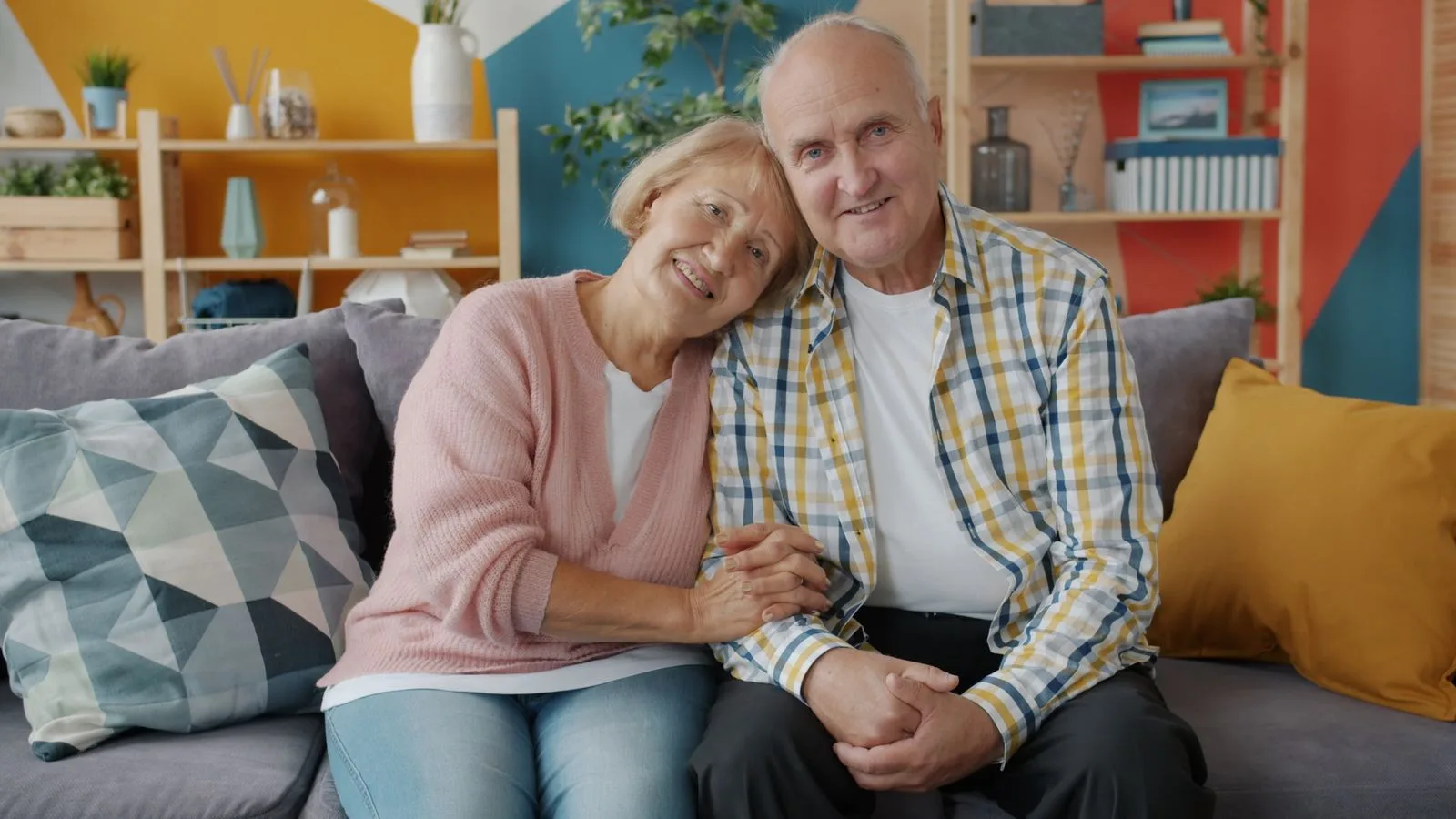 Smiling elderly couple seated together on a cozy sofa in a colorful living room.