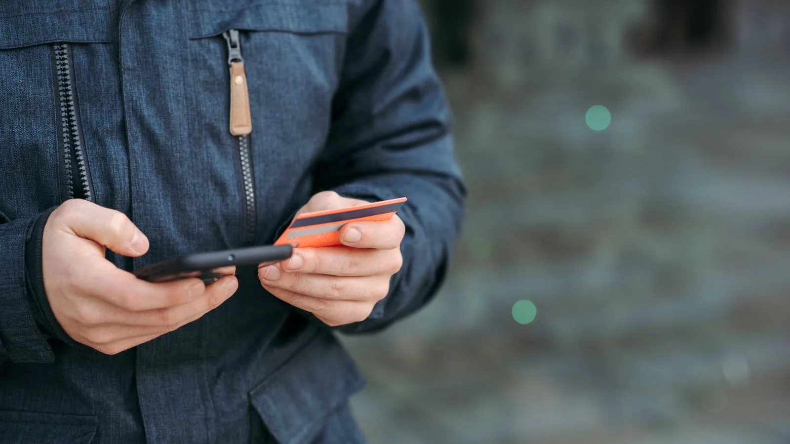 Crop anonymous male in casual clothes entering credit card details on smartphone on street in daylight