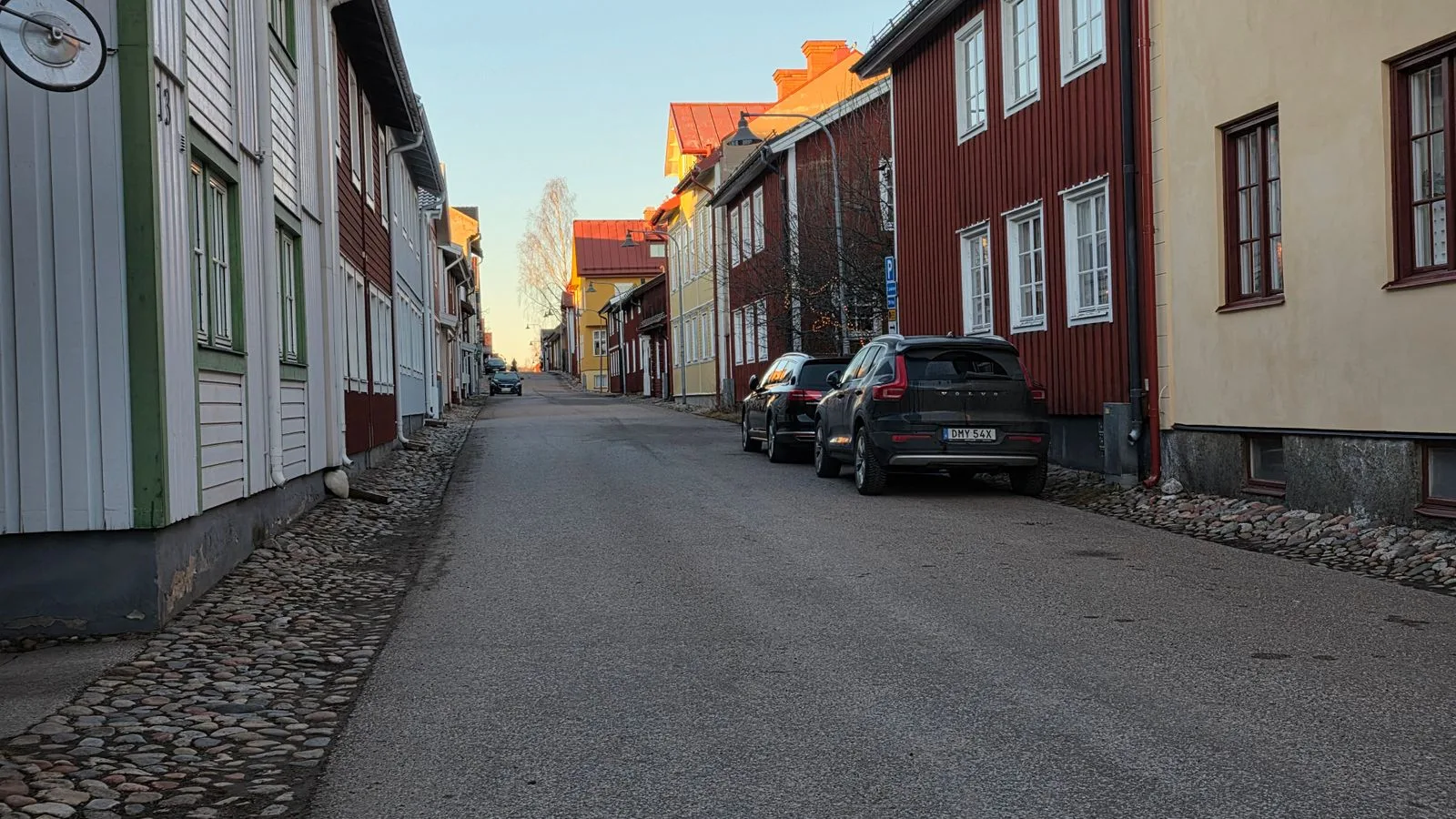 Quiet European street with traditional wooden houses and parked cars on a sunny day.