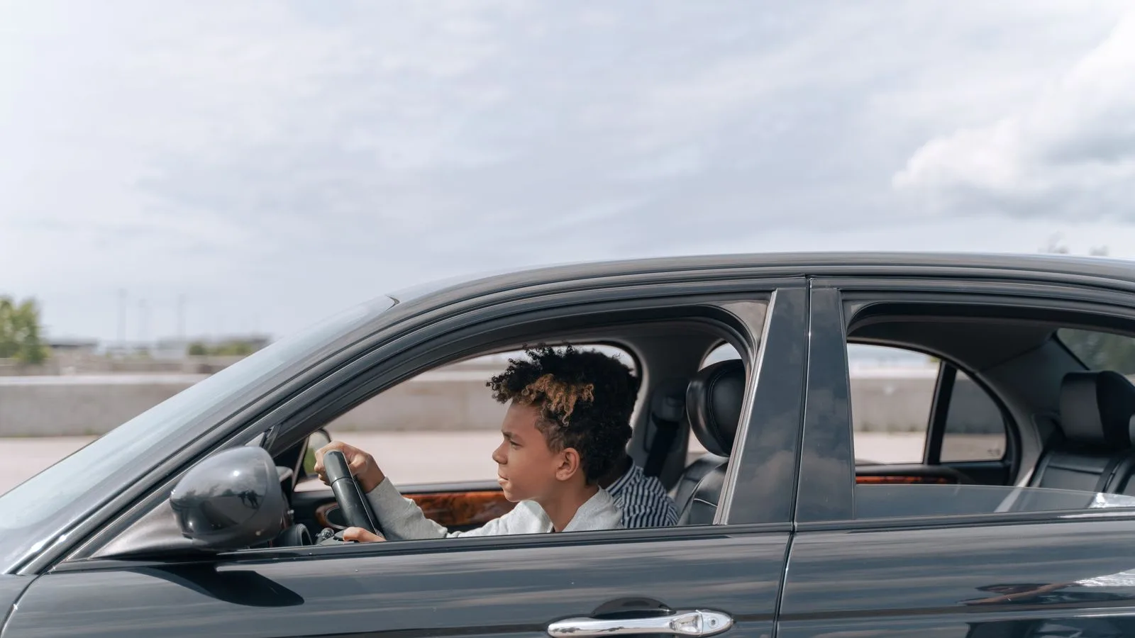 Side view of a young male teenager focused on driving a car in bright daylight.