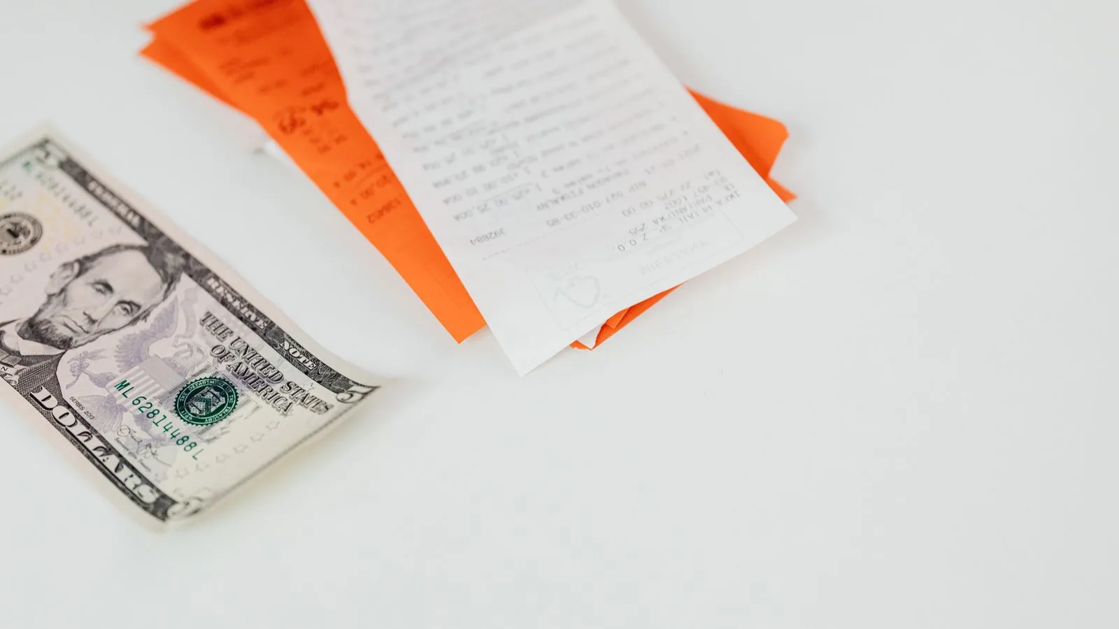 A five dollar bill and receipts on a white surface, emphasizing finance and expenses.