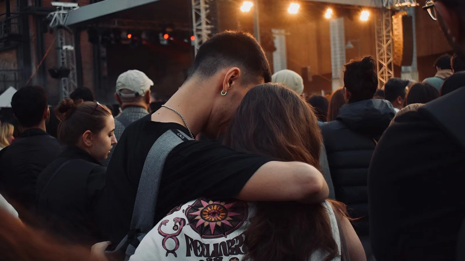 A young couple embraces at an outdoor music festival during the evening.