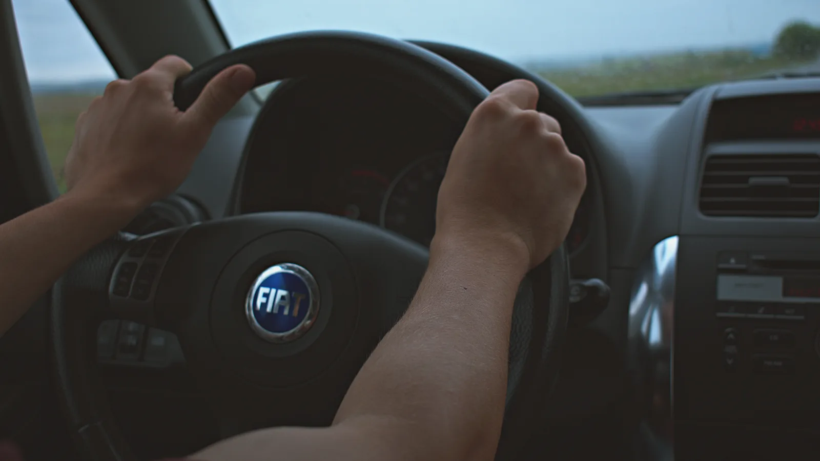 Close-up of hands on the steering wheel of a Fiat car interior, perfect for travel and automotive themes.