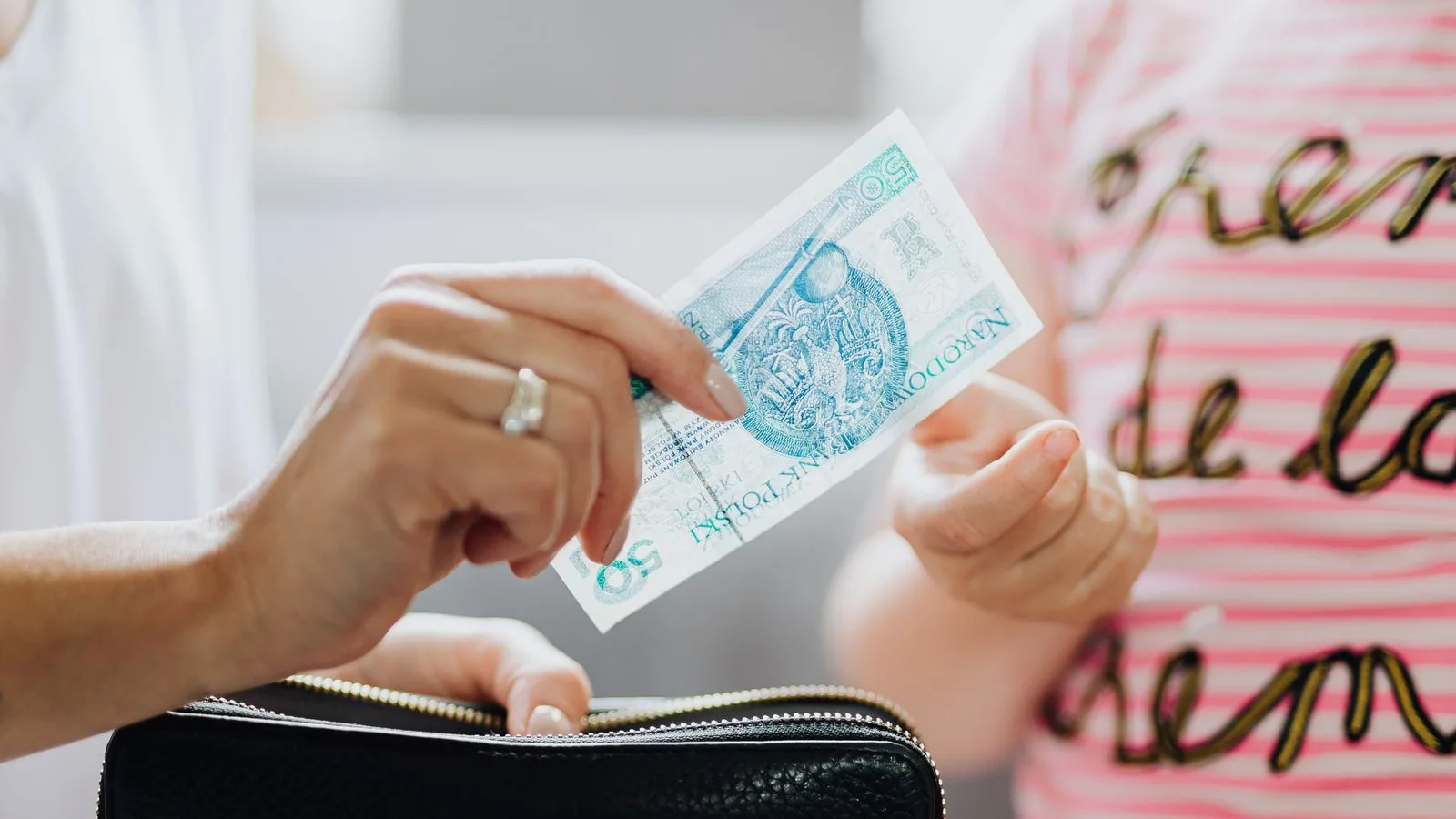 Close-up of hands exchanging a 50 Polish zloty note, highlighting financial transaction.