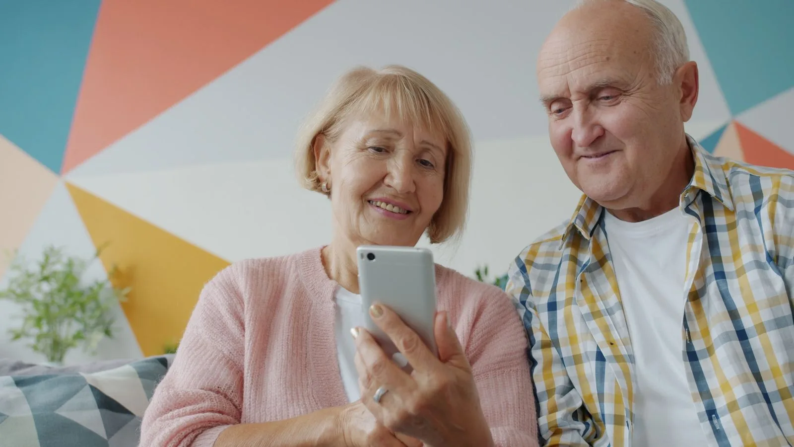 Happy senior couple using smartphone together on couch at home, enjoying technology.