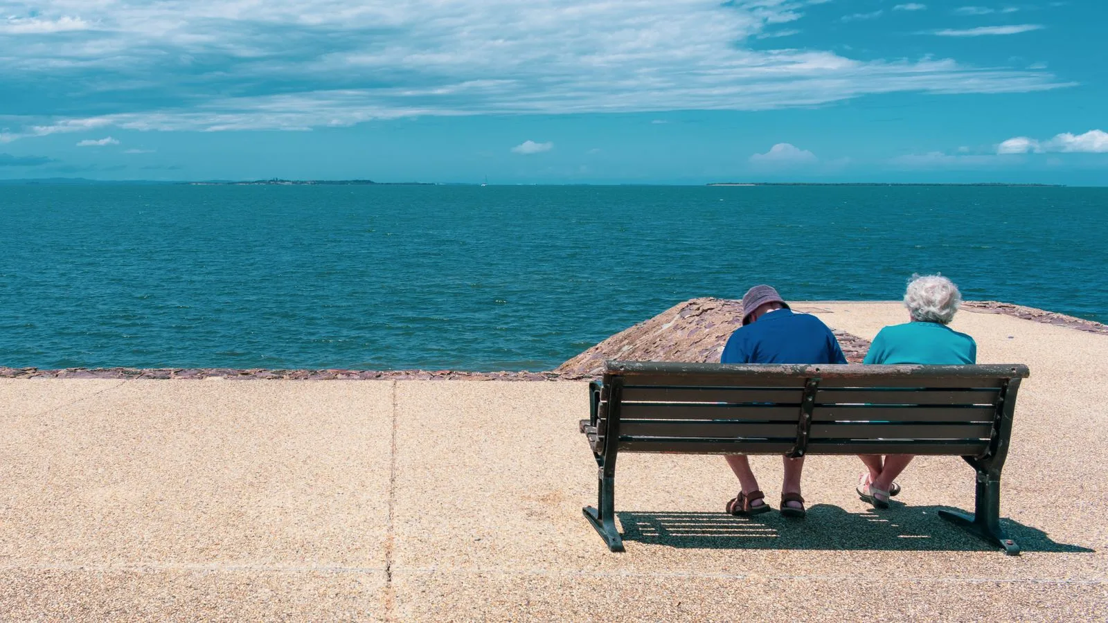 Senior couple relaxing on a seaside bench, enjoying a sunny summer day overlooking the ocean.