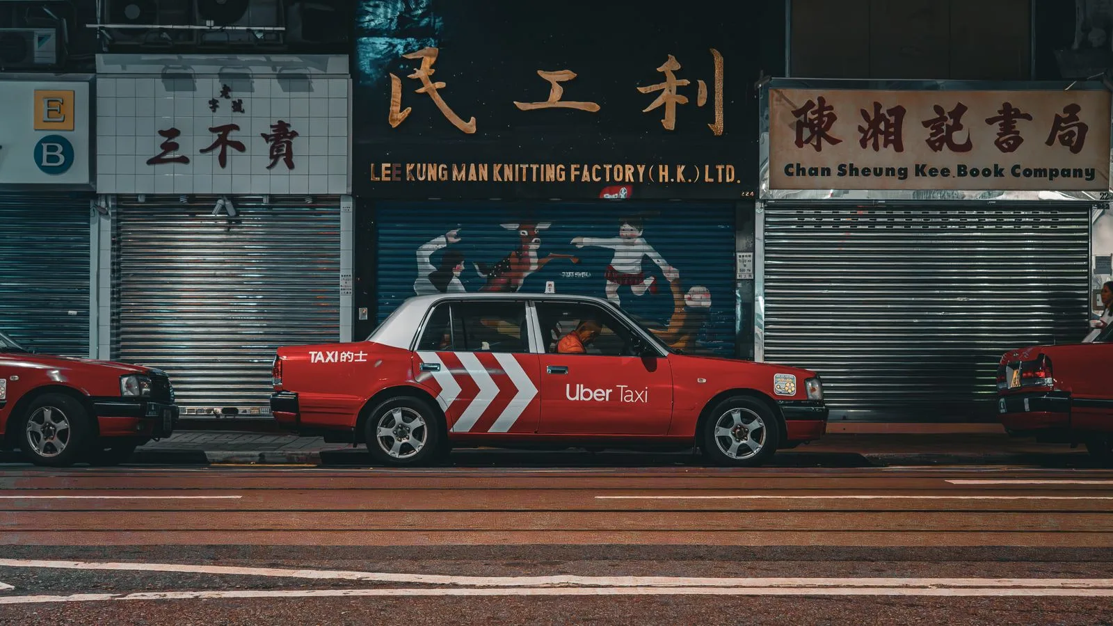 Red Uber Taxi parked on a vibrant Hong Kong city street at night.