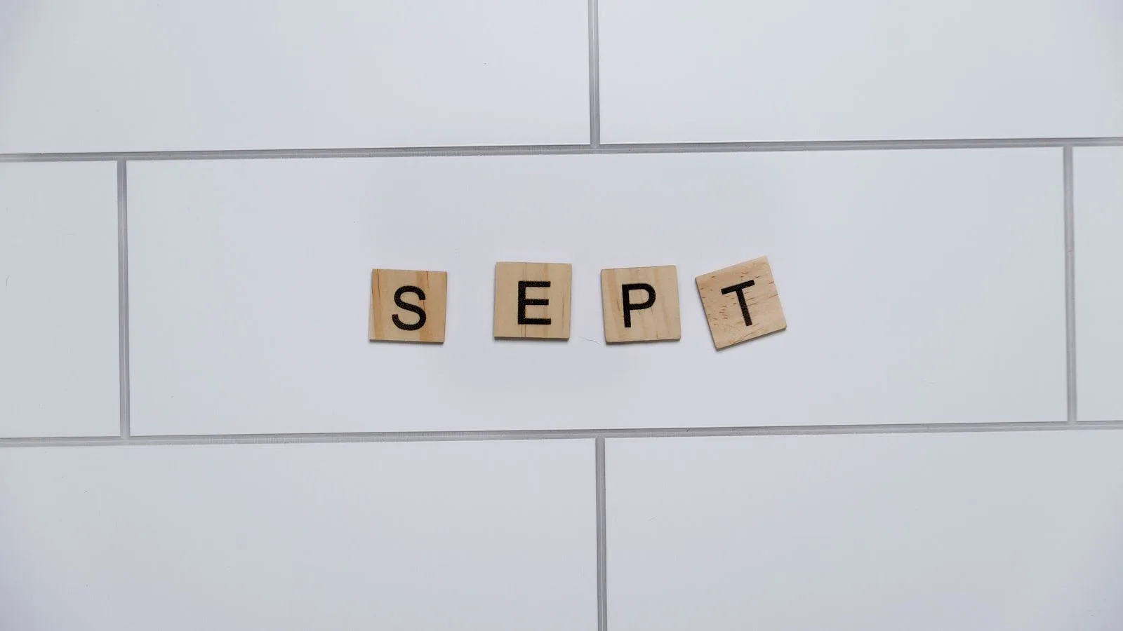 Wooden letter tiles spelling 'Sept' on a white tiled background, perfect for marking calendar events.