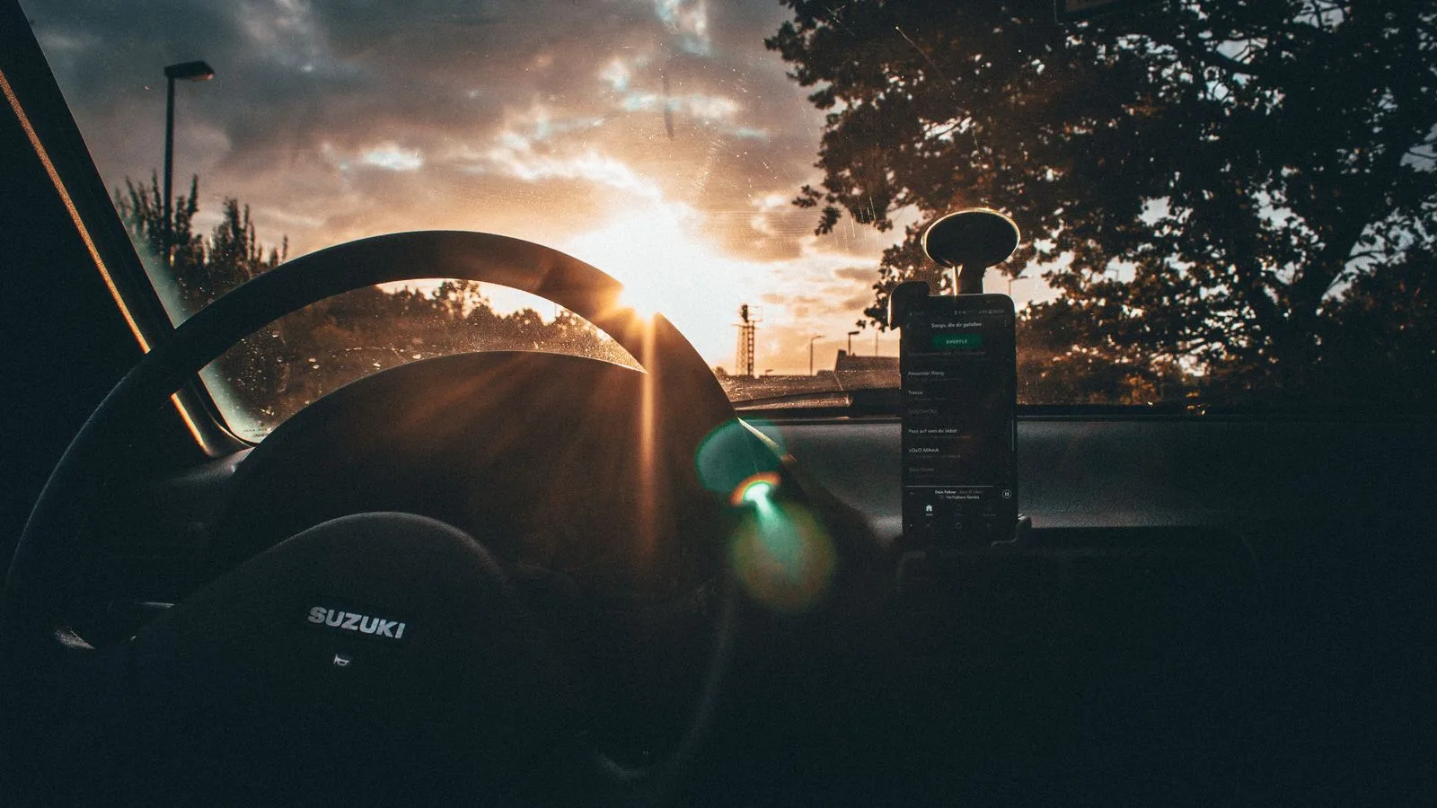 View of sunrise through a car windshield with steering wheel and smartphone visible.