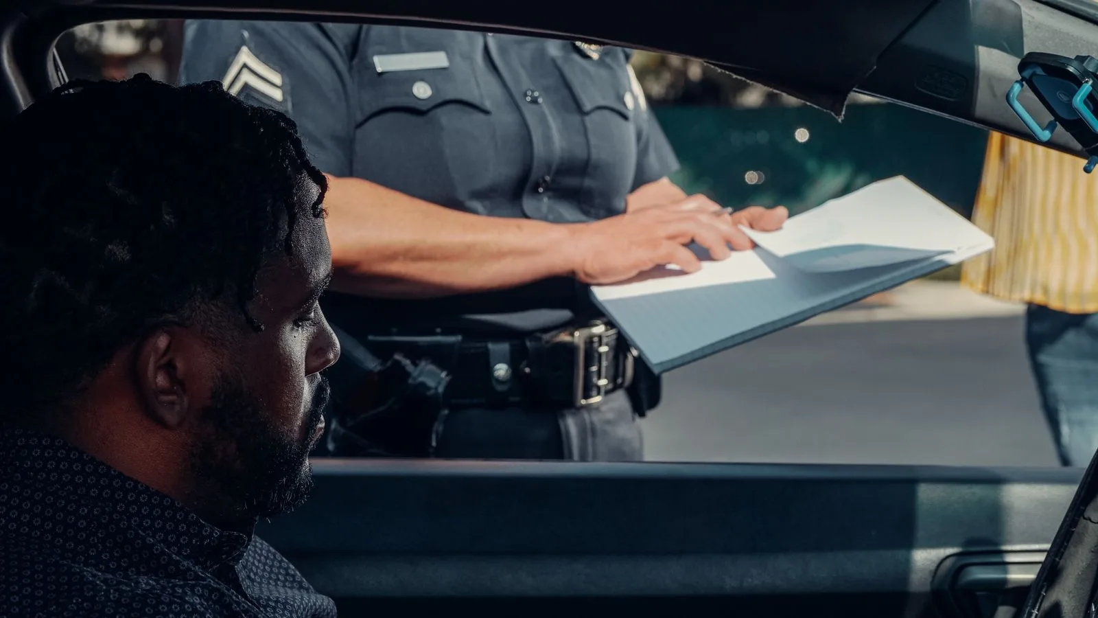 A police officer issues a traffic ticket to a man in a car. Close-up view of the interaction through the window.