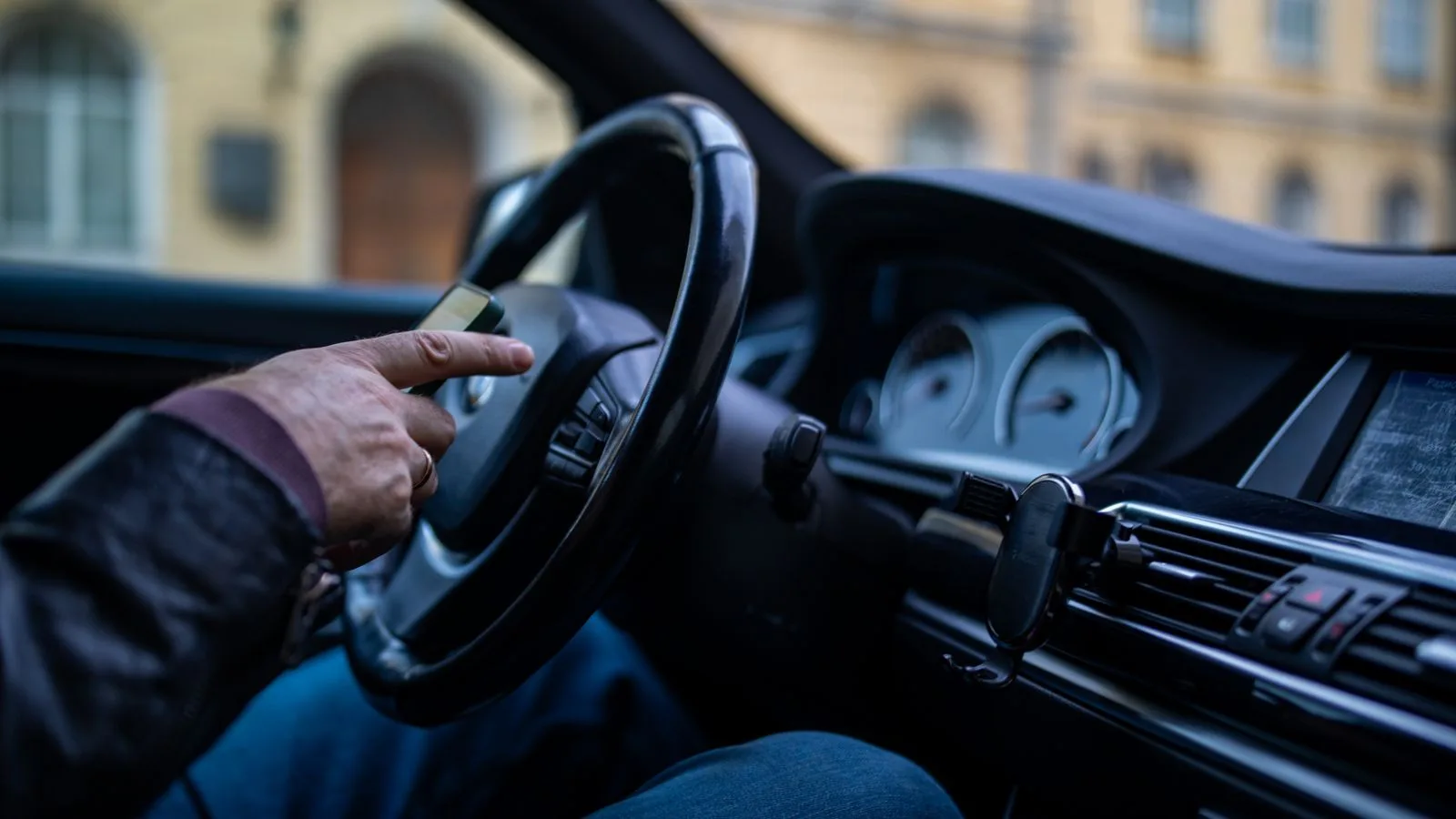 A man in a car interior using a smartphone while driving, emphasizing modern technology and lifestyle.