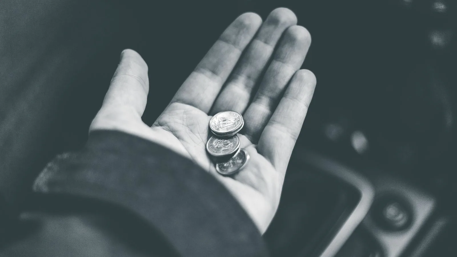 Black and white crop anonymous person demonstrating shiny coins while sitting in car on blurred background