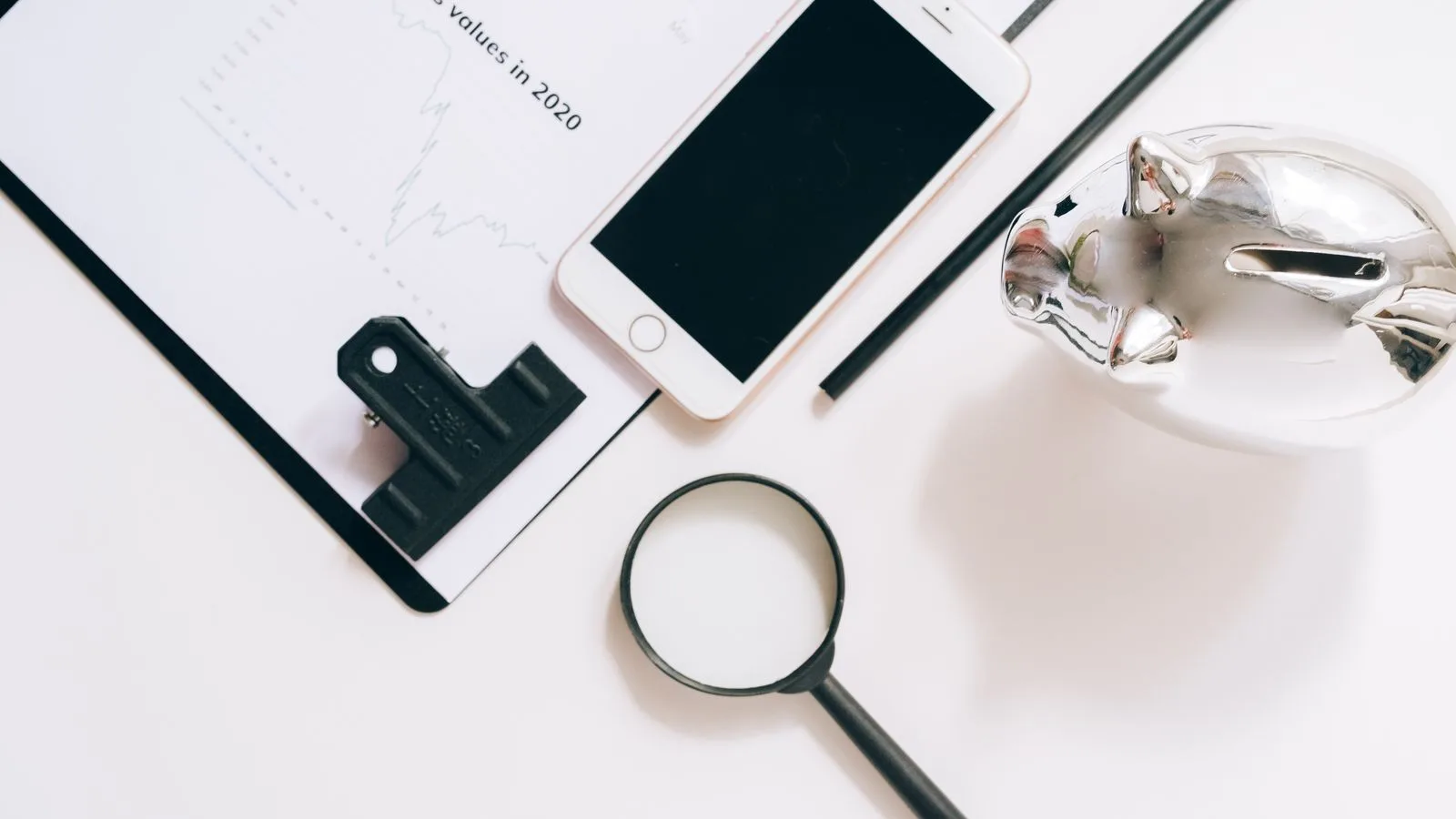 A flat lay of financial documents with a smartphone, magnifying glass, and piggy bank.