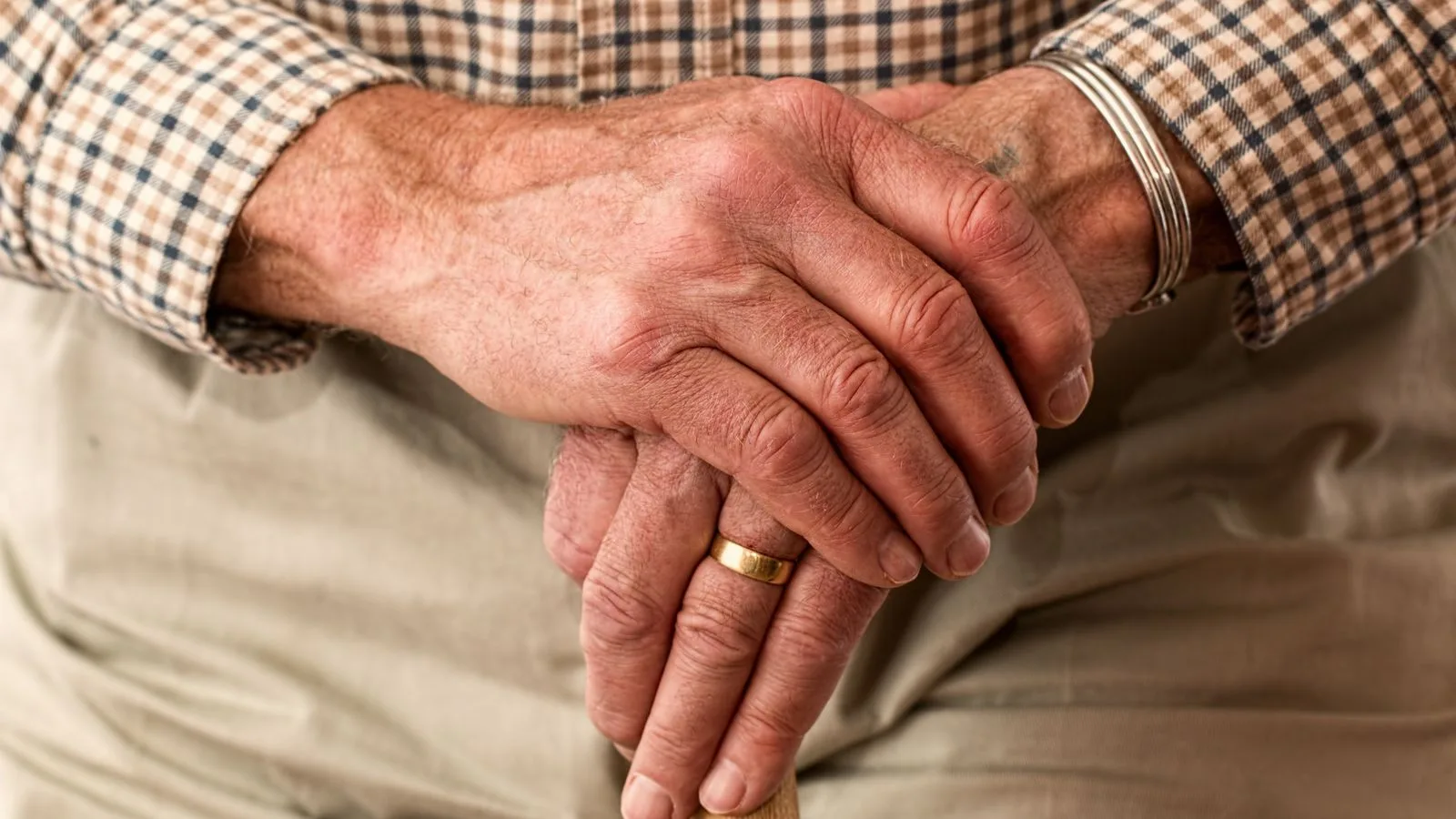 A detailed image of elderly hands clasping a wooden cane, symbolizing aging and support.