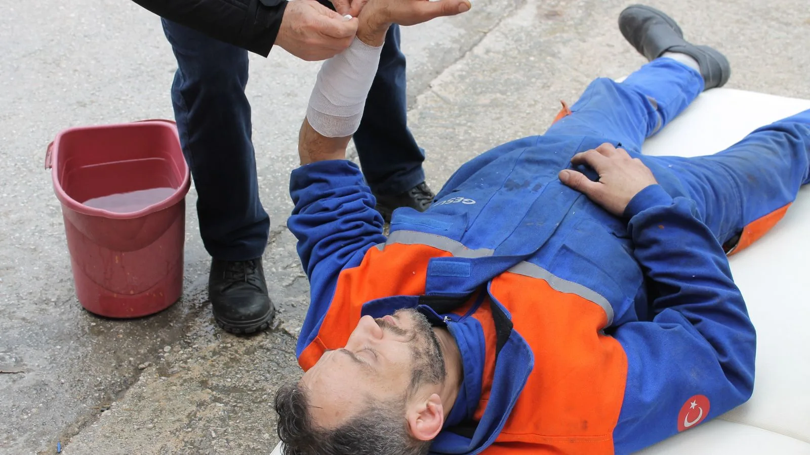 Injured worker receiving first aid on-site with arm bandage applied.