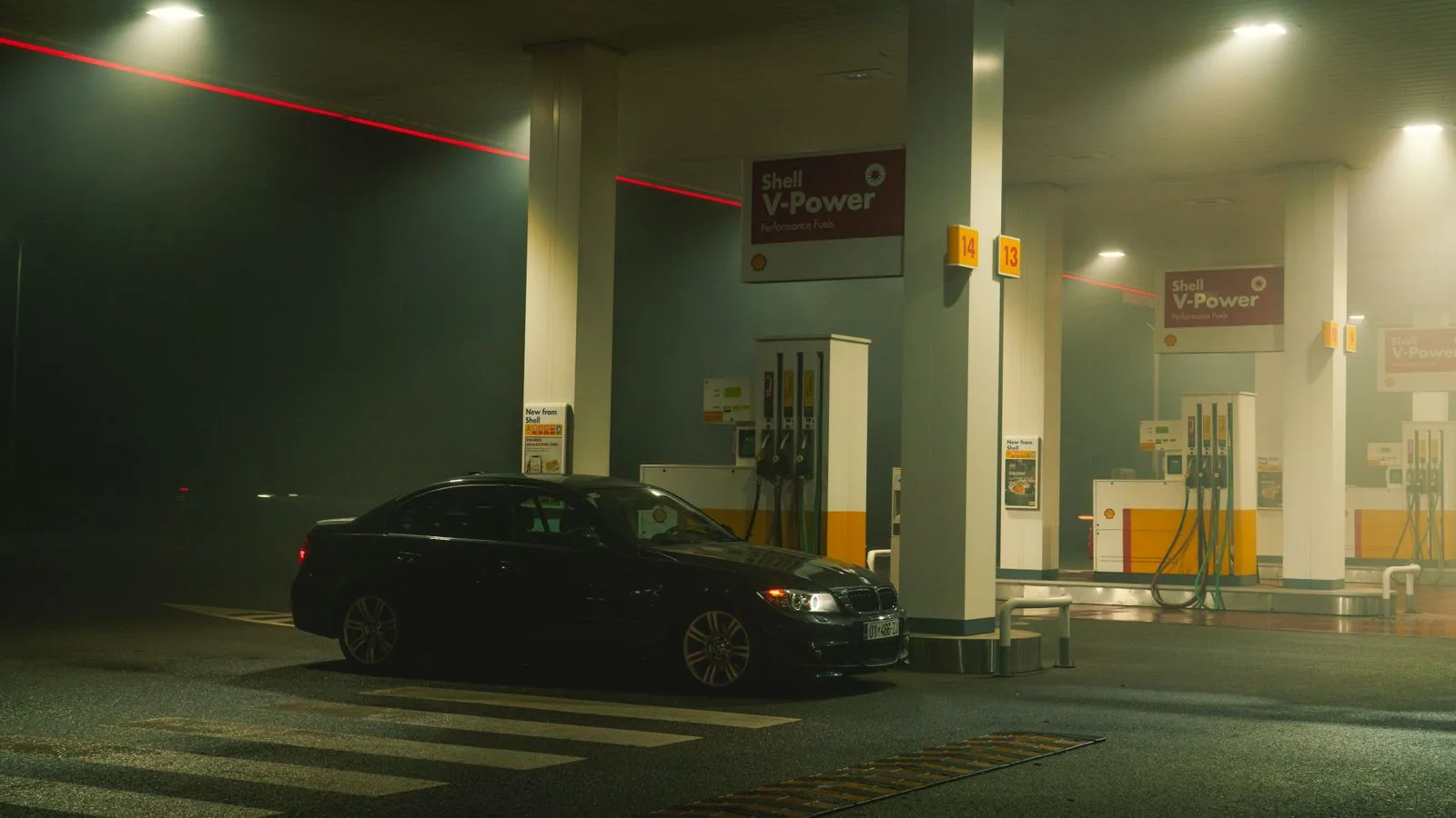 A BMW sports car parked at a Shell gas station at night, featuring bright lights and an urban setting.