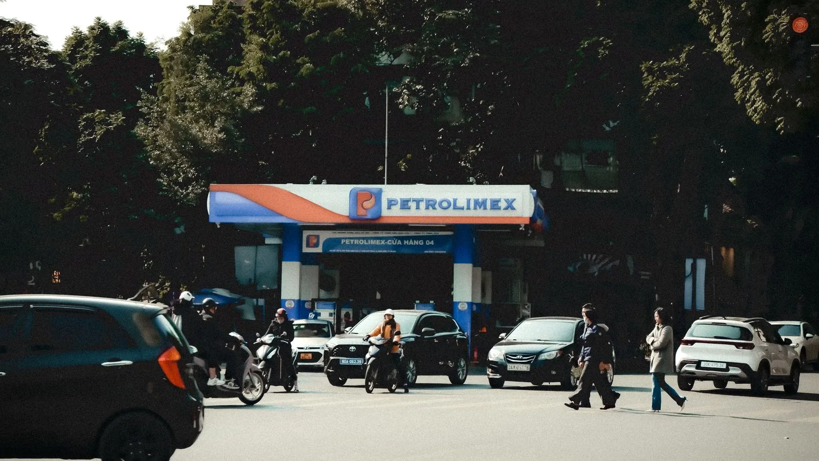 Busy street scene with vehicles and pedestrians at a Petrolimex gas station under daylight.