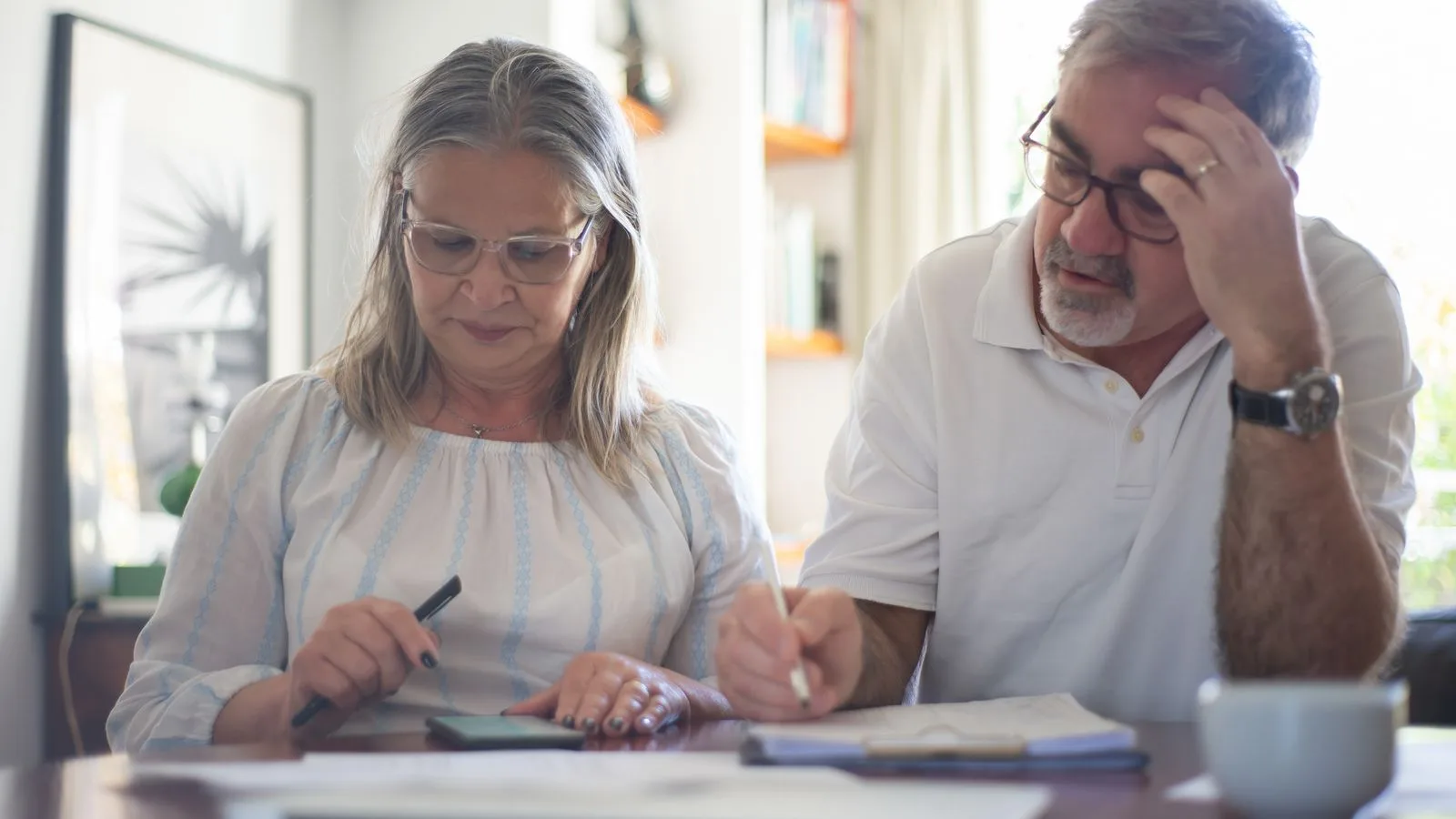Senior couple calculating expenses at home office desk with documents and notes.