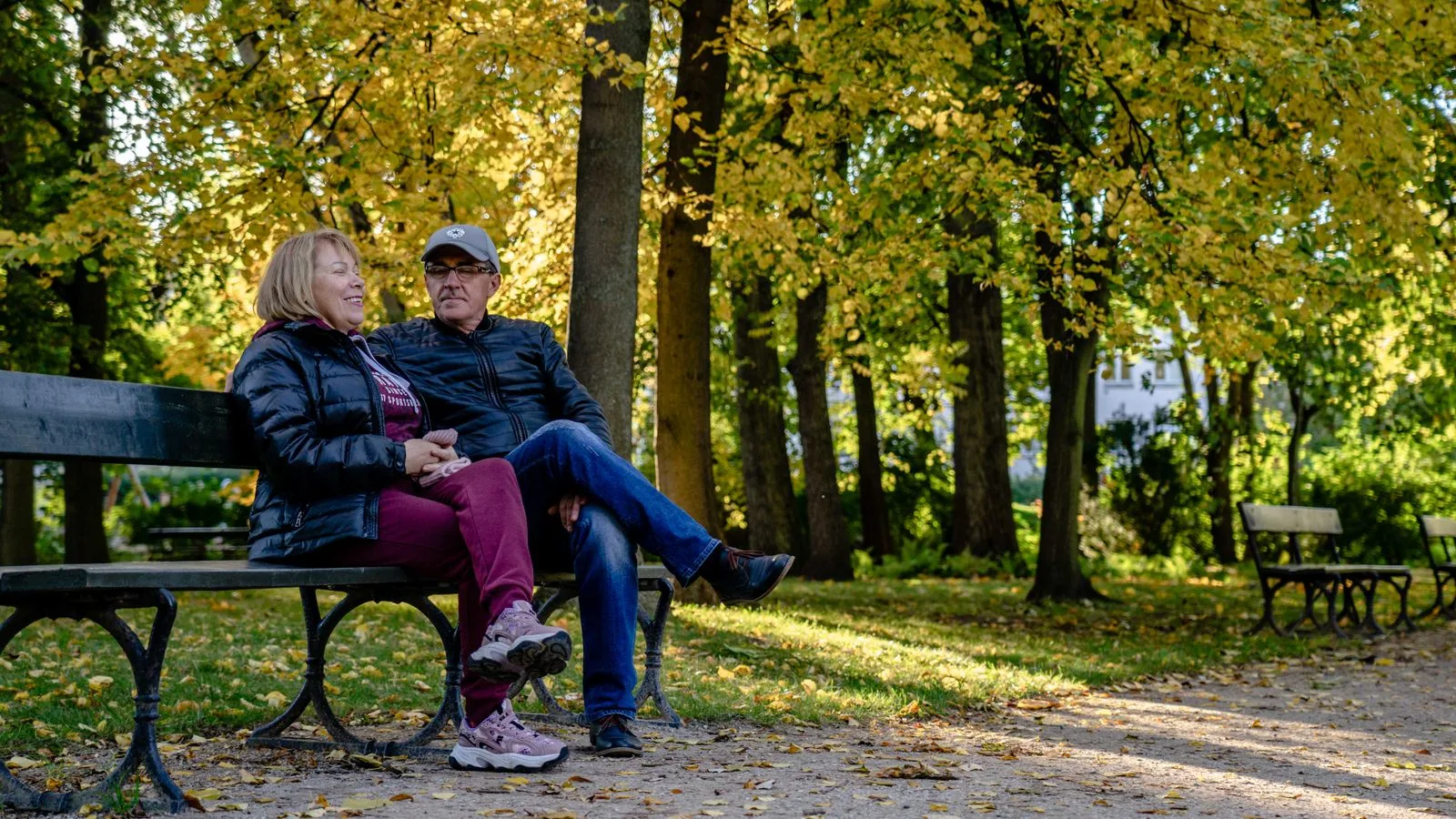 Happy senior couple sitting on a park bench surrounded by autumn foliage.