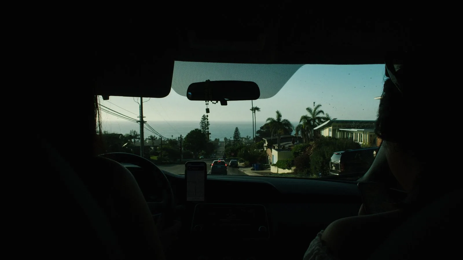 View from a car on a coastal road, showing lush greenery and ocean horizon.