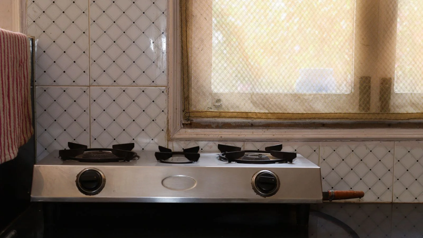 Stainless steel stove in home kitchen with tiled wall and window view.