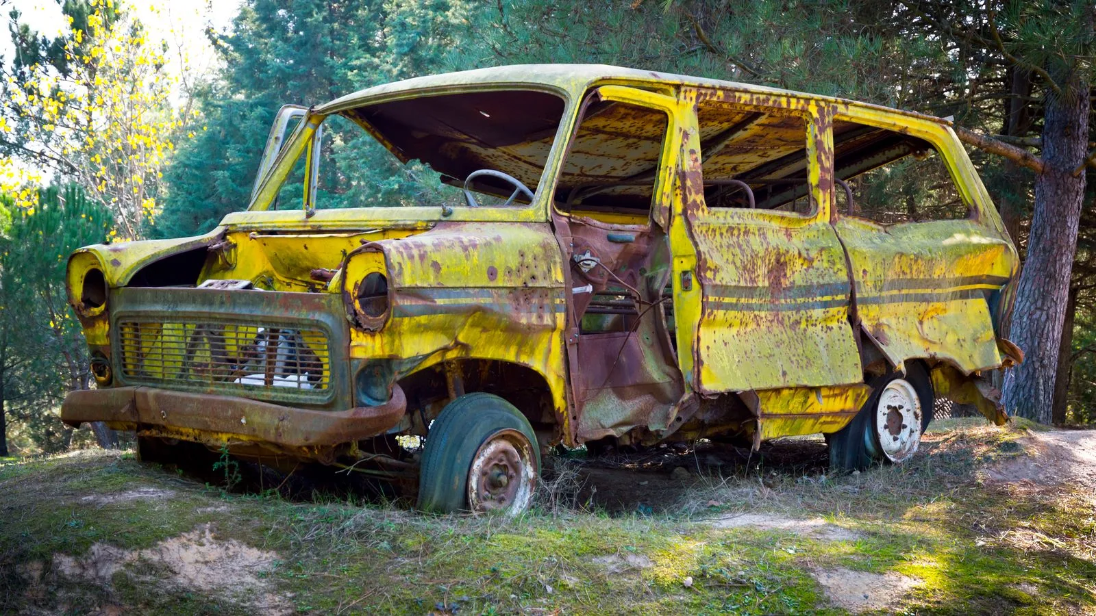 Old rusted yellow minibus abandoned in a lush green forest.