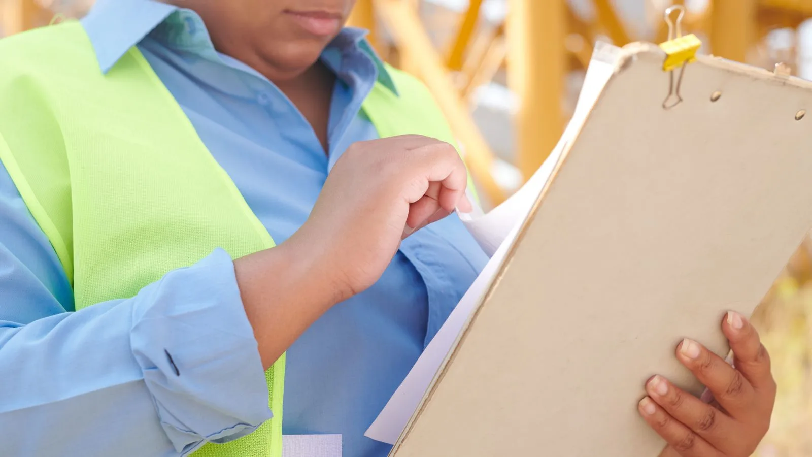 A female engineer in safety gear reviewing documents on a clipboard at a construction site.