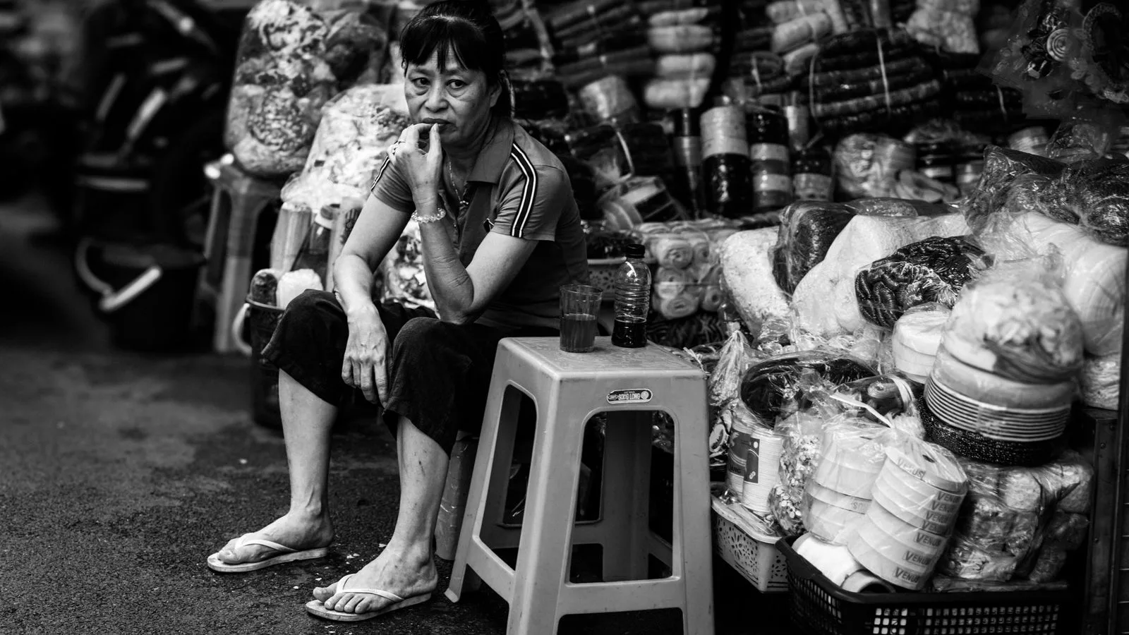 Street vendor sitting among goods in a Hanoi market, Vietnam, showcasing local commerce and lifestyle.