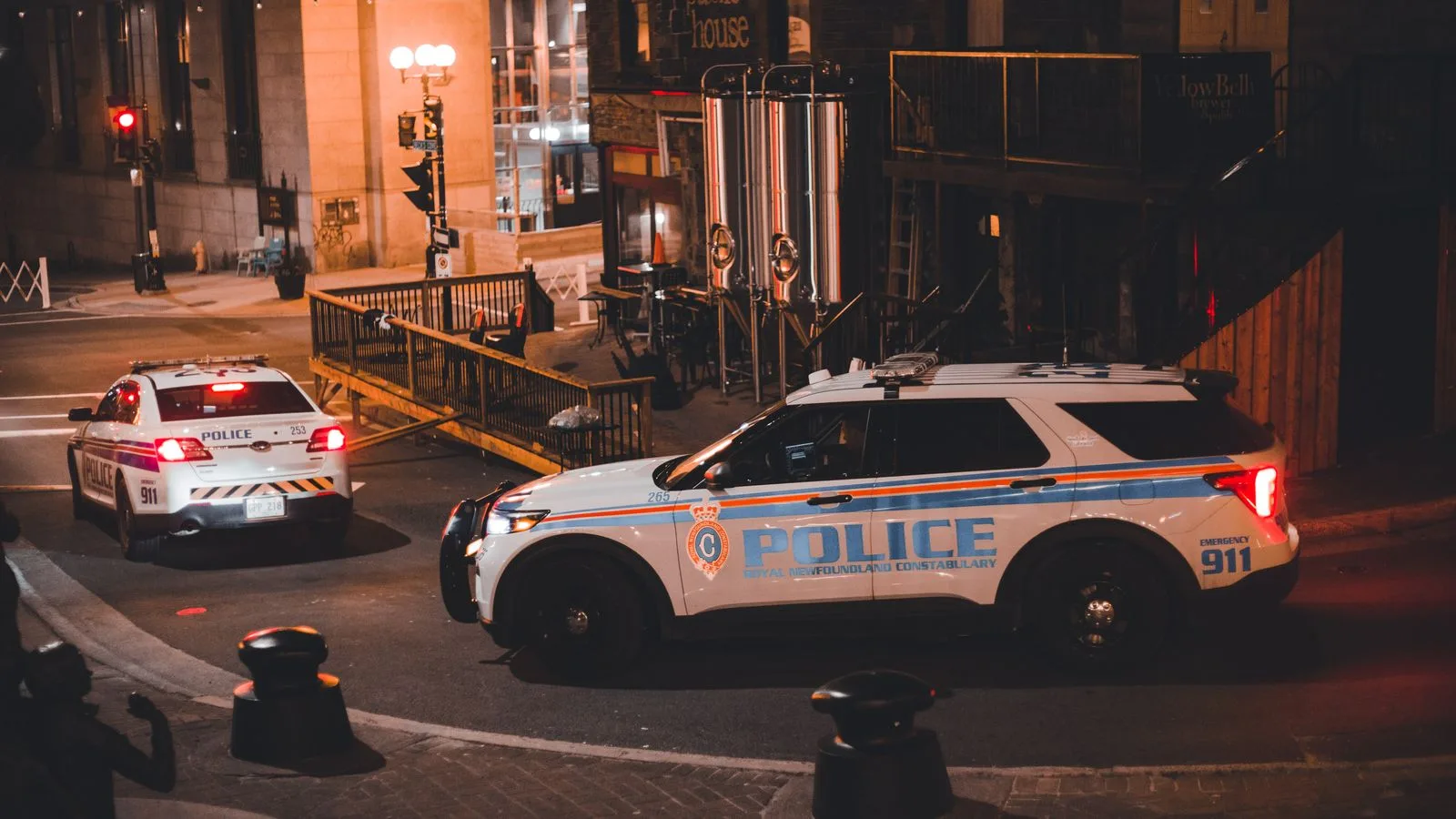 Two police cars patrolling a city street at night with warm lighting creating a dramatic urban mood.