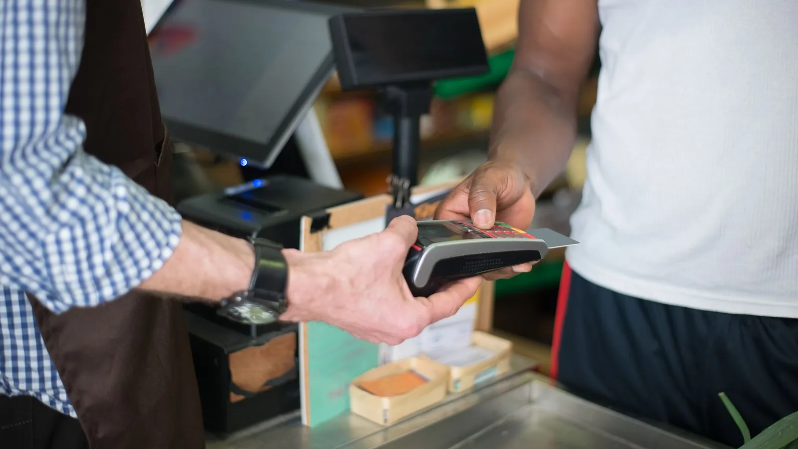 A customer making a payment with a credit card at a store checkout counter using a card reader.