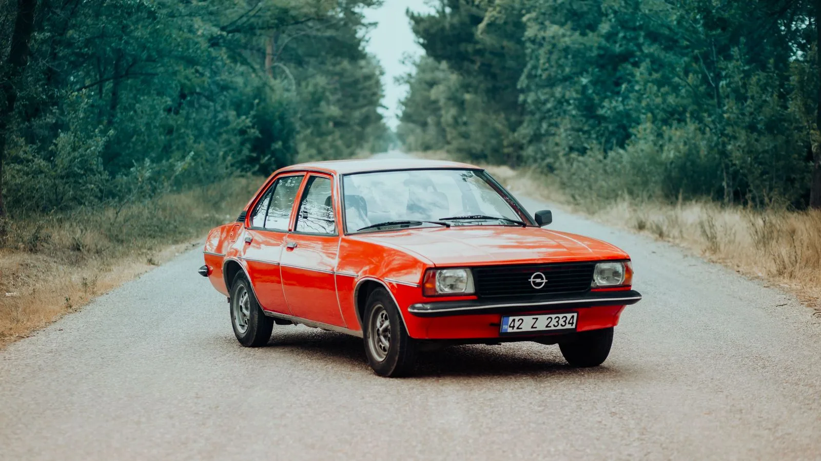Vintage orange car parked on a tranquil rural road surrounded by lush greenery in Konya, Türkiye.