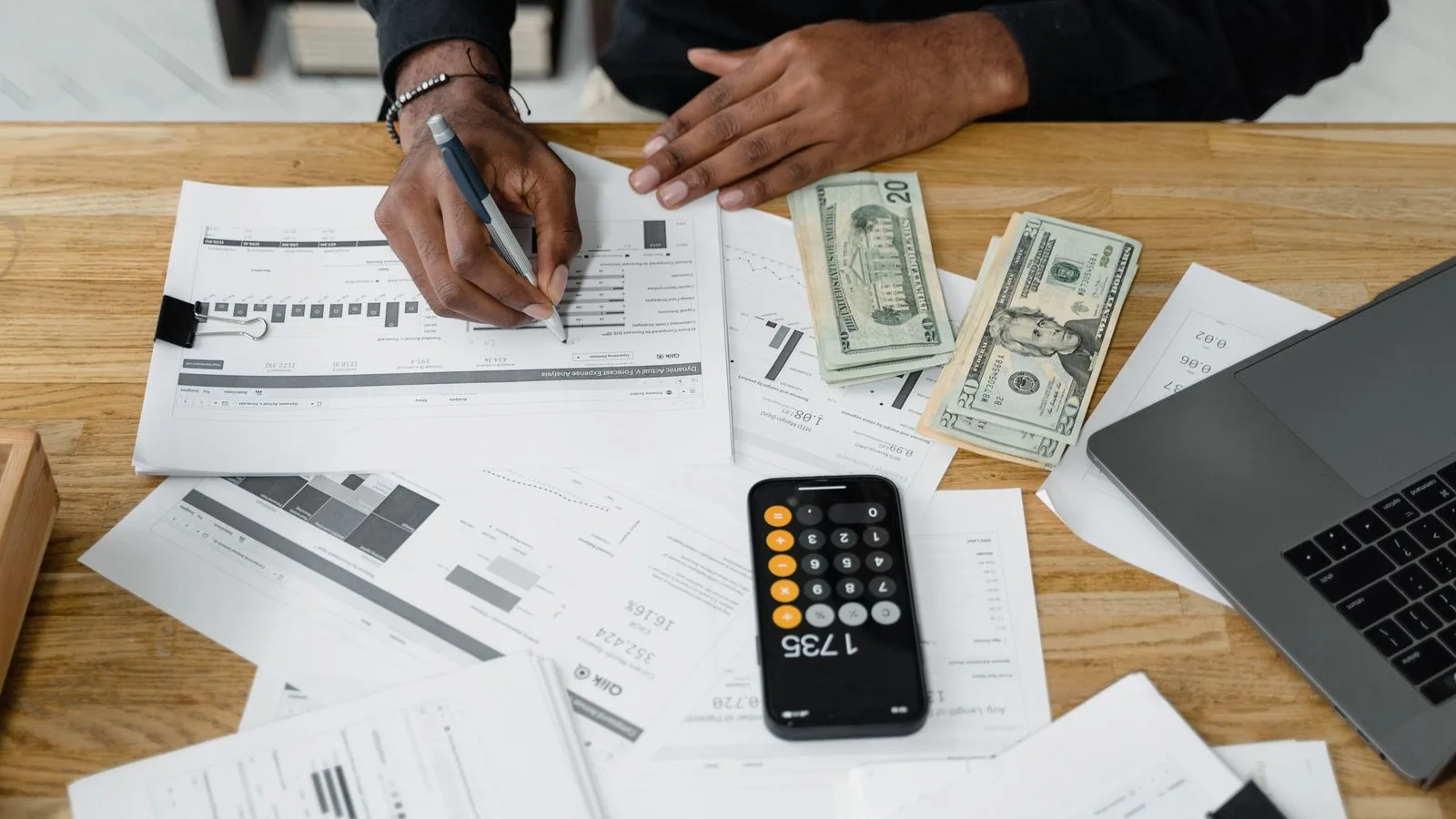 Man working on financial reports with calculator, money, and laptop on a desk.