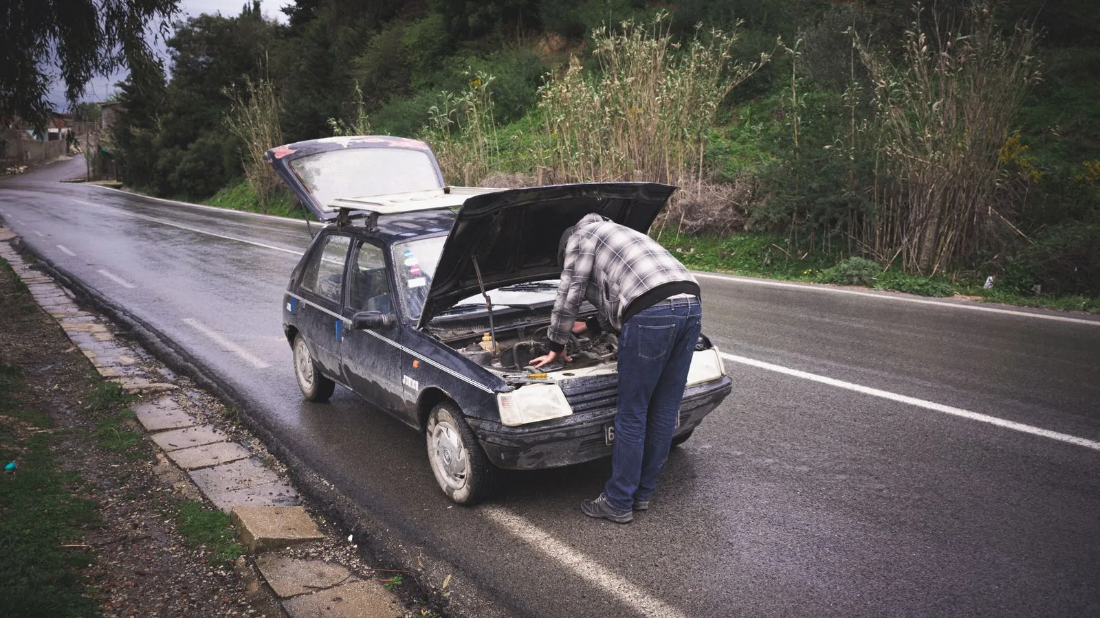 An individual repairing a car on a rainy road in Tabarka, showcasing urgent roadside vehicle maintenance.