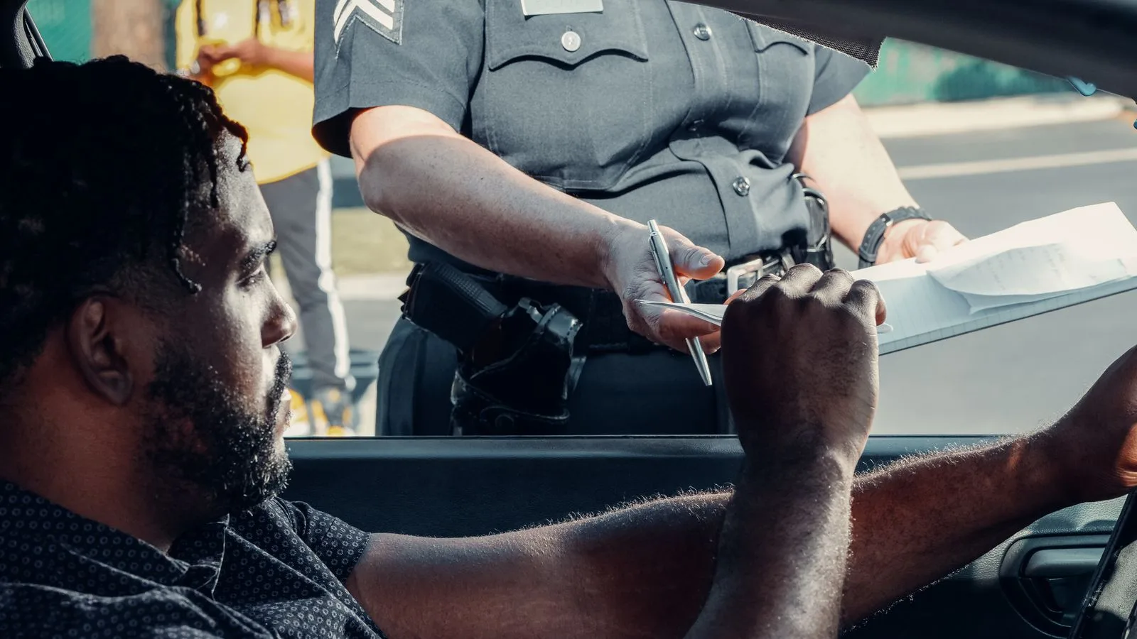 Police officer handing a traffic ticket to a driver during roadside inspection.
